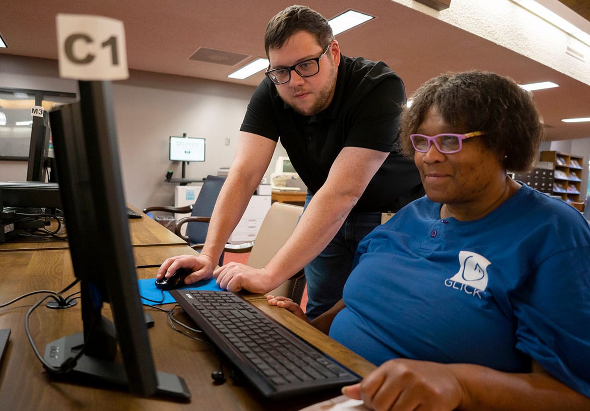 Library volunteer helping patron use computer